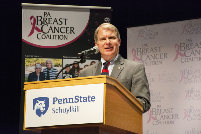 Senator David Argall speaks at a podium with Penn State Schuylkill's logo on the front. A backdrop with the Pennsylvania Breast Cancer Coalition logo is erected behind him.