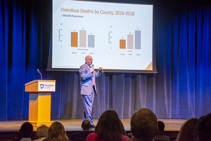 Schuylkill County District Attorney Mike O'Pake delivers a presentation, standing in front of a slide that examines drug overdose deaths by county between 2016-18