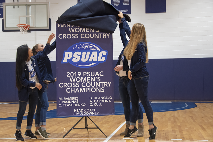 Members of the Women's Cross country team are shown unveiling their championship banner.
