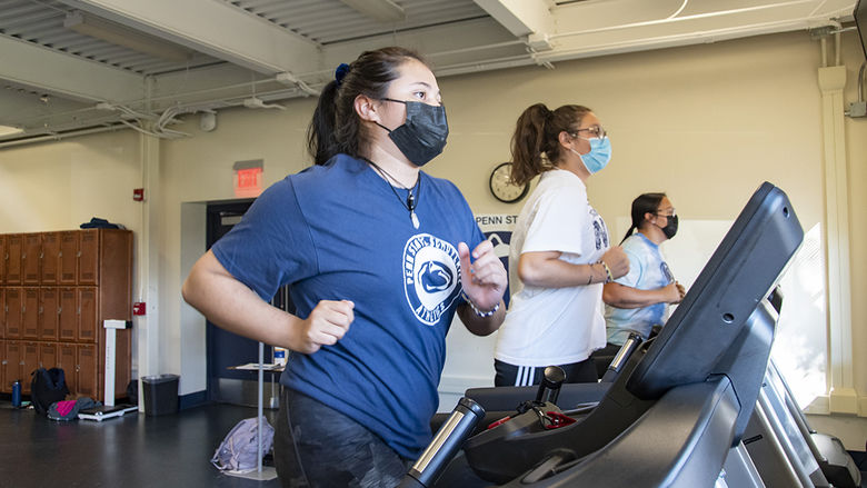 Girls wearing masks, sweatpants, and t-shirts run on treadmills.