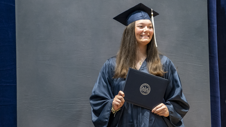 A female graduate poses with diploma.