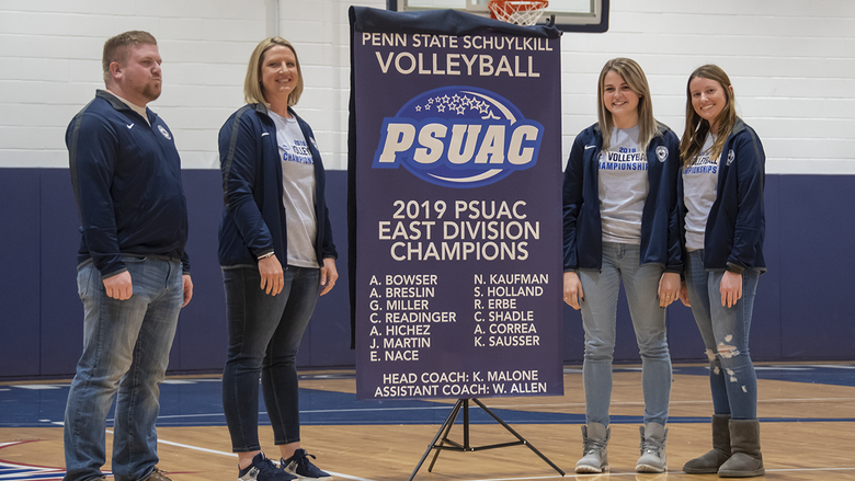 members of the Women's Volleyball team stand with the championship banner.