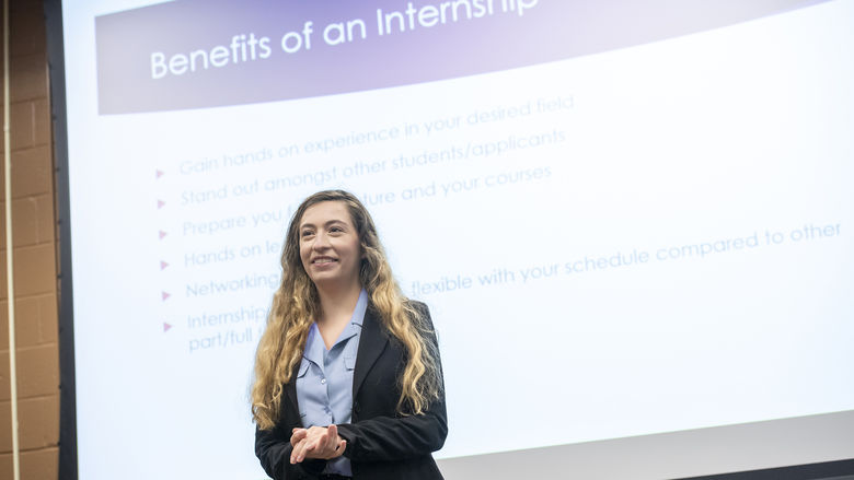 Student in business attire standing in front of PowerPoint presentation about internships