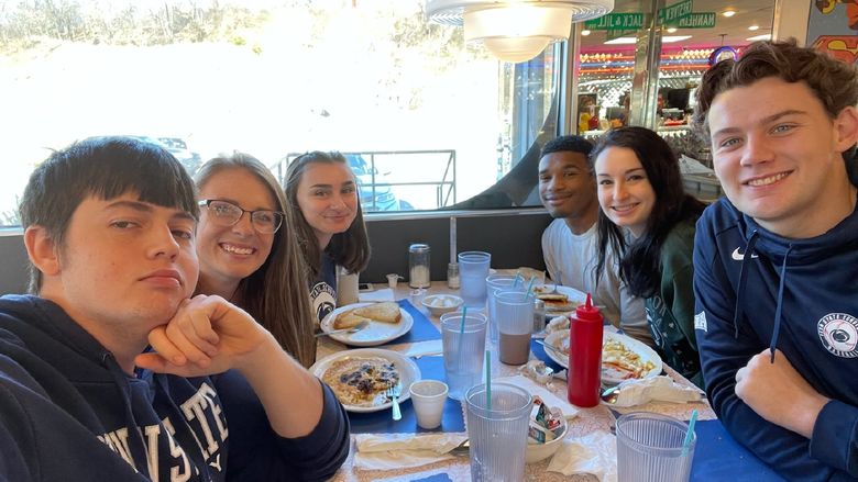 six students sit at a diner table with breakfast food between them