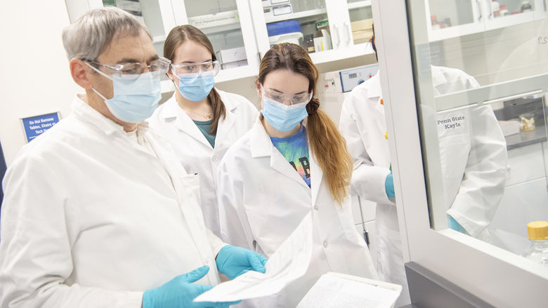 Three people wearing white lab coats, latex gloves, and masks in a chemistry lab