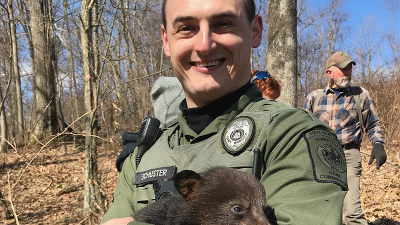 An image of game warden holding a infant bear.