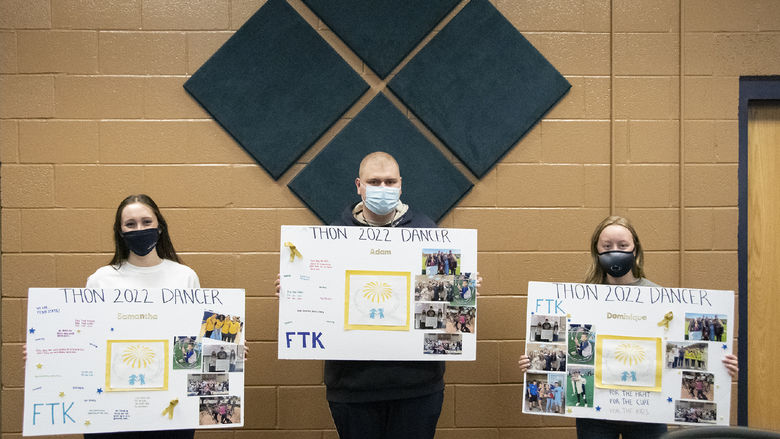 Three students wearing masks stand with 24" x 36" posters with photos and their names on them