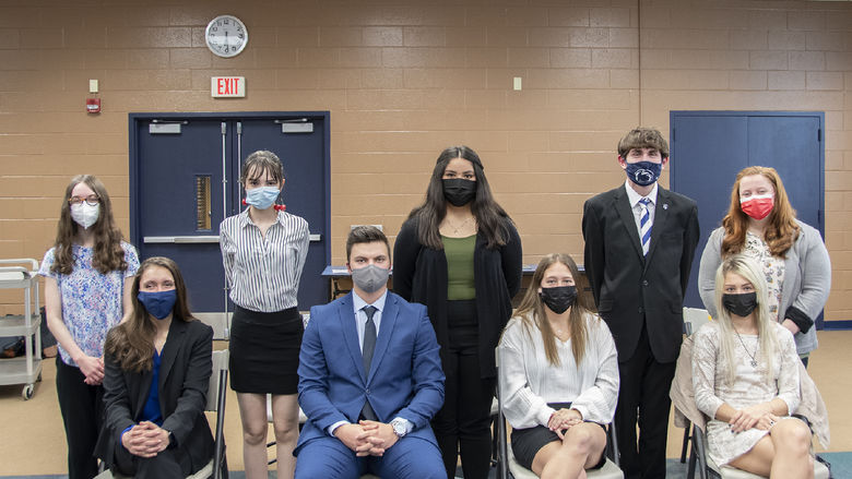 Nine students wearing masks and business formal clothing pose for a photo.