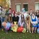 Students wearing Halloween costumes and holding balloons pose for a photo in front of a brick building