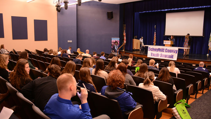 Students from 15 area schools listen to students speak at the podium.