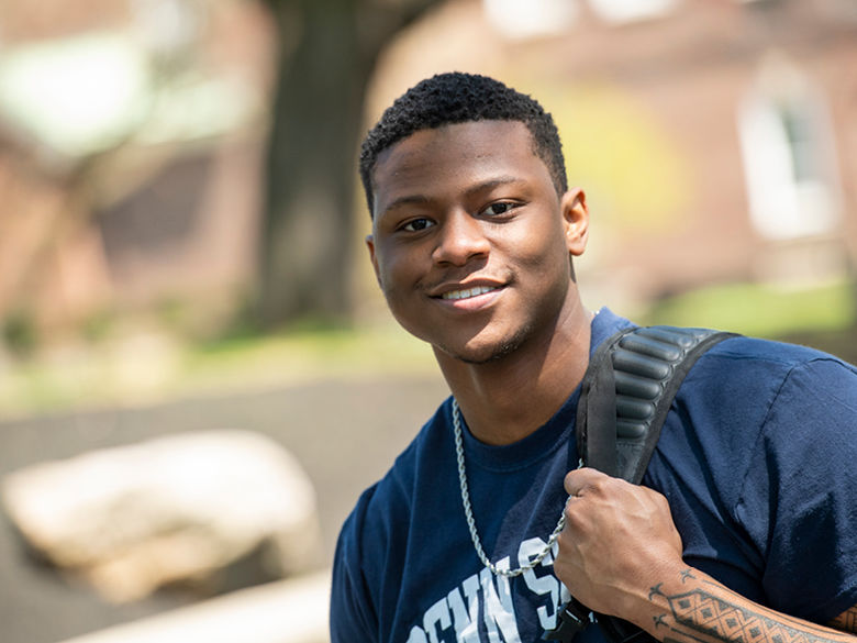 Photo of smiling student Quon Banks wearing navy blue Penn State t-shirt with chain necklace and backpack over his shoulder