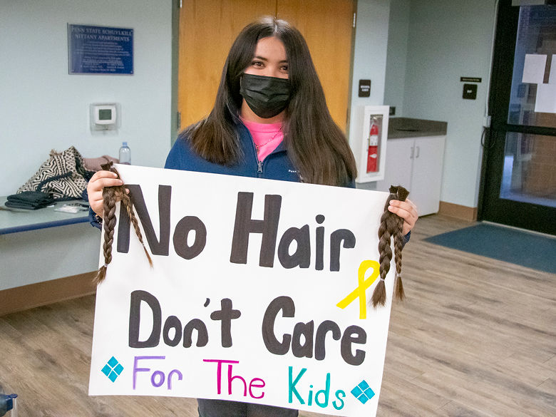 Girl wearing face mask and holding braided hair with sign that reads "No hair, don't care, for the kids."
