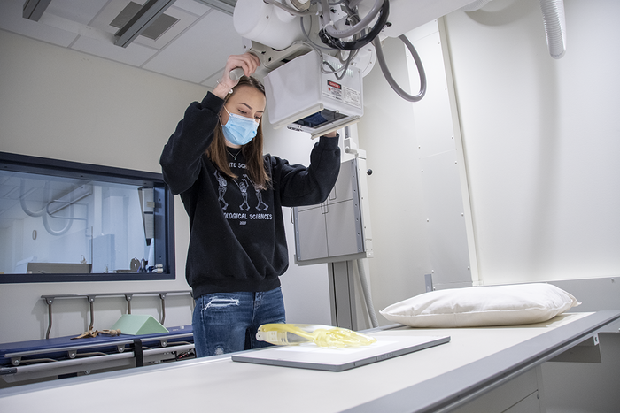 Student wearing a black sweatshirt and surgical mask while operating a digitized radiographic unit
