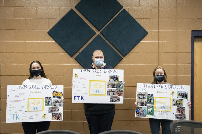 Three students wearing masks stand with 24" x 36" posters with photos and their names on them