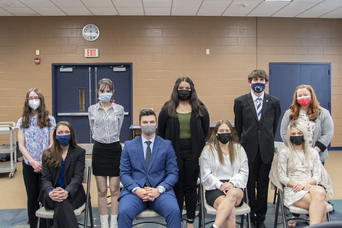 Nine students wearing masks and business formal clothing pose for a photo.