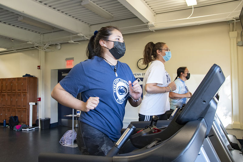 Girls wearing masks, sweatpants, and t-shirts run on treadmills.