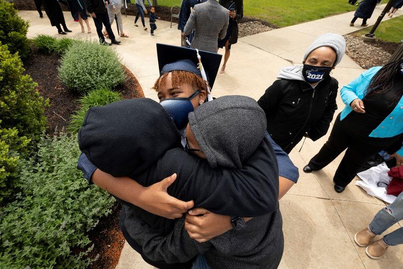 woman in mask and graduation cap hugging two people