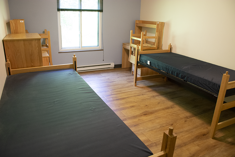 Two twin XL beds and two wooden desks line the walls of a bedroom in the Nittany I Apartments with a window between them.
