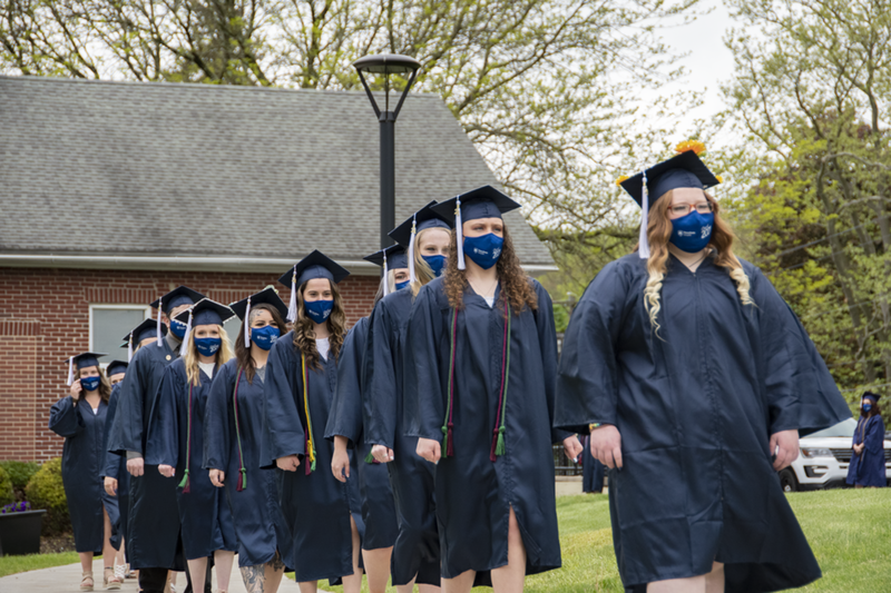 Students in academic regalia walking down a sidewalk at Penn State Schuylkill.