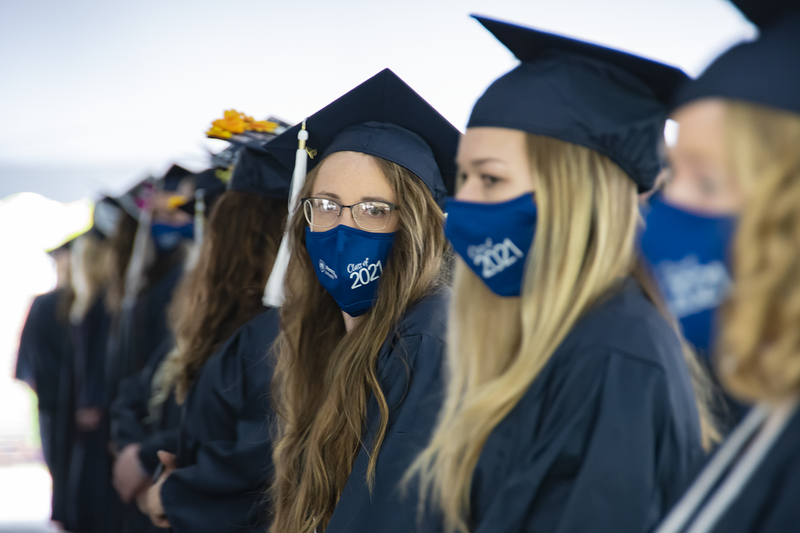 Students wearing face masks and academic regalia wait to be seated.