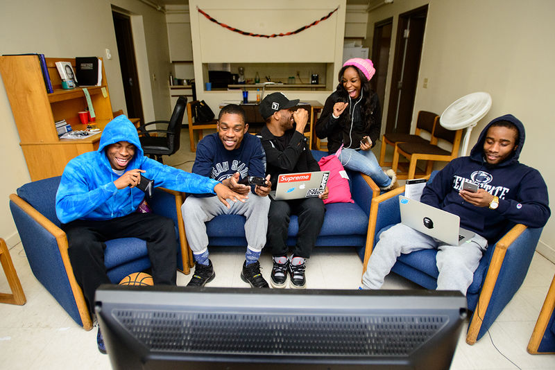 A group of students play Xbox, some look at their phones, others fist bump