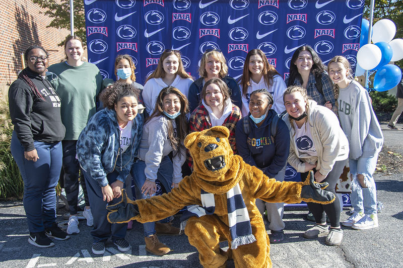 Group of smiling girls pose for a photo in front of a blue background with Penn State Athletics and NAIA logos.