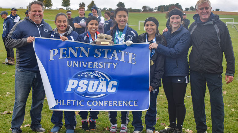 Penn State Schuylkill cross country runners pose with a "Penn State PSUAC" sign and lion shrine.