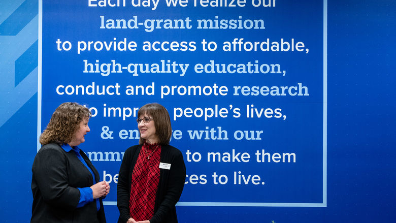 Two women talk in front of a blue wall