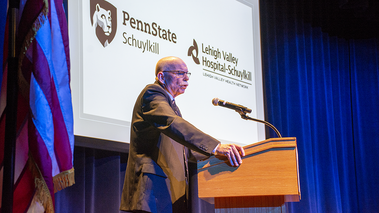 Bill Rowan delivers his presentation in front of a projected image of Penn State Schuylkill and Lehigh Valley Hospital - Schuylkill logos