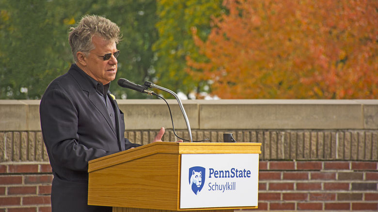 A man wearing all black with sunglasses speaks while standing at a podium