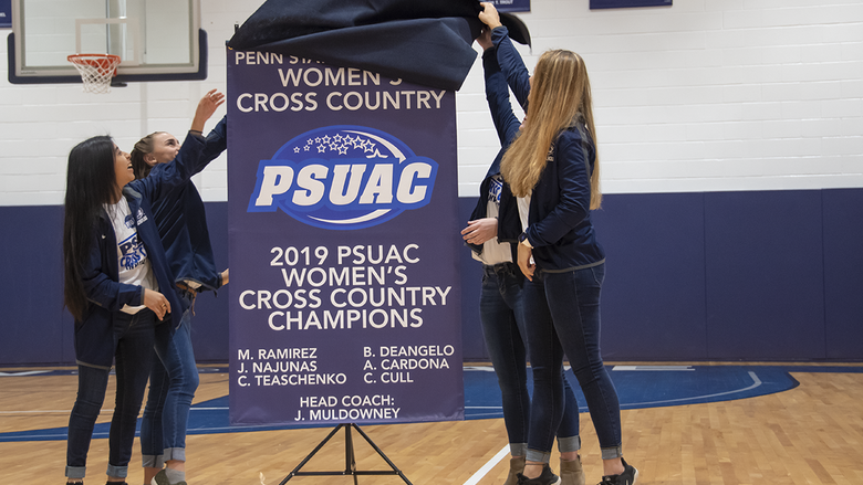 Members of the Women's Cross country team are shown unveiling their championship banner.