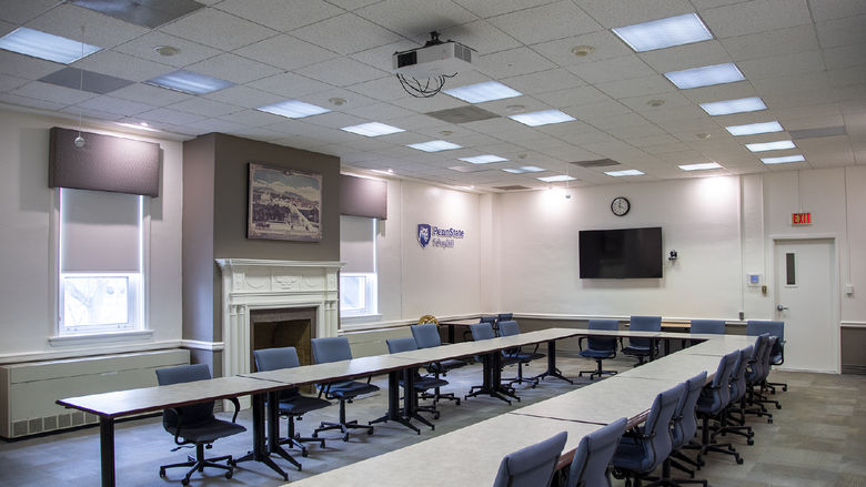 Board room with long white tables in a U-shape, blue chairs on wheels, and a fireplace.