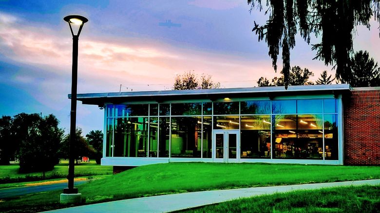 Penn State Schuylkill's glassy Student Community Center sits atop green grass during sunset hours