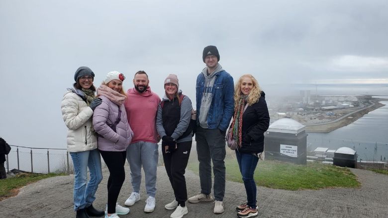 six people stand on a sidewalk overlooking a lower area