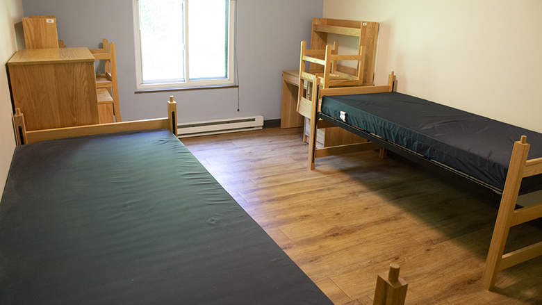 Two twin XL beds and two wooden desks line the walls of a bedroom in the Nittany I Apartments with a window between them.
