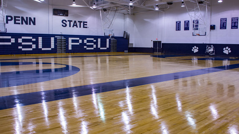 Wooden gymnasium floor with reflection of overhead fluorescent lights and bleachers on the side of the wall
