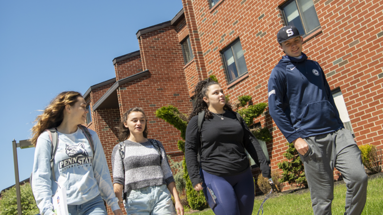 Four students walk together outside of student housing complex.