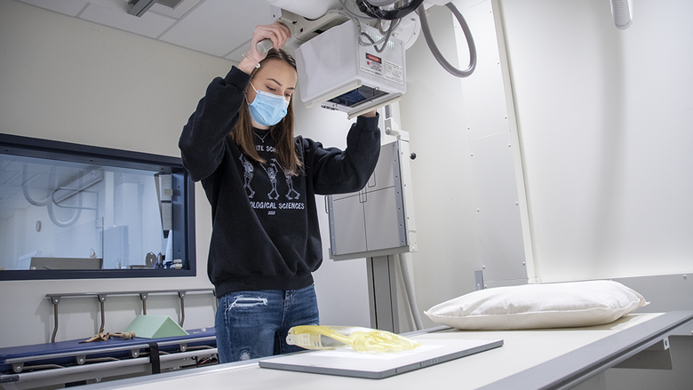 Student wearing a black sweatshirt and surgical mask while operating a digitized radiographic unit