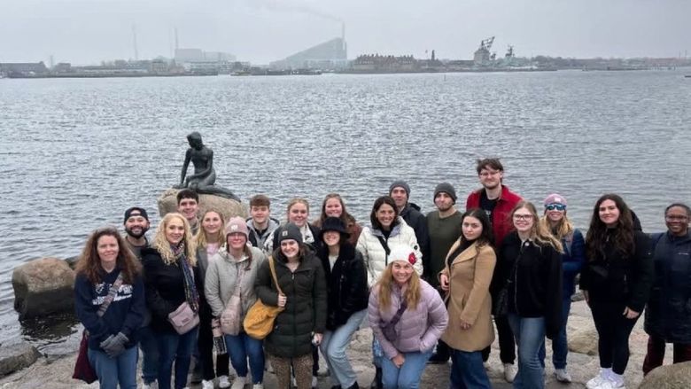 a group of people stand with the little mermaid statue in the background