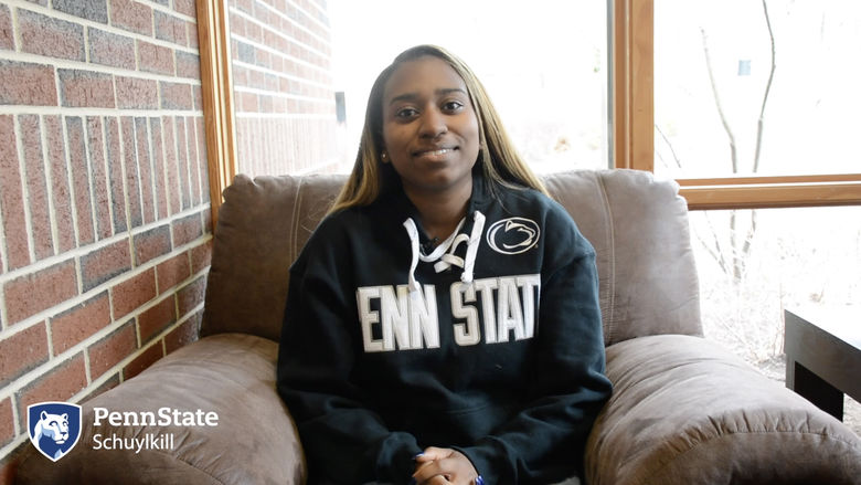 Girl in Penn State hoodie sits on a brown armchair in front of a bright window.