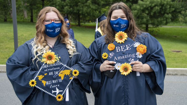 Students wearing academic regalia holding decorated mortarboards.