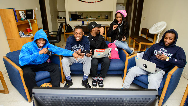 A group of students play Xbox, some look at their phones, others fist bump