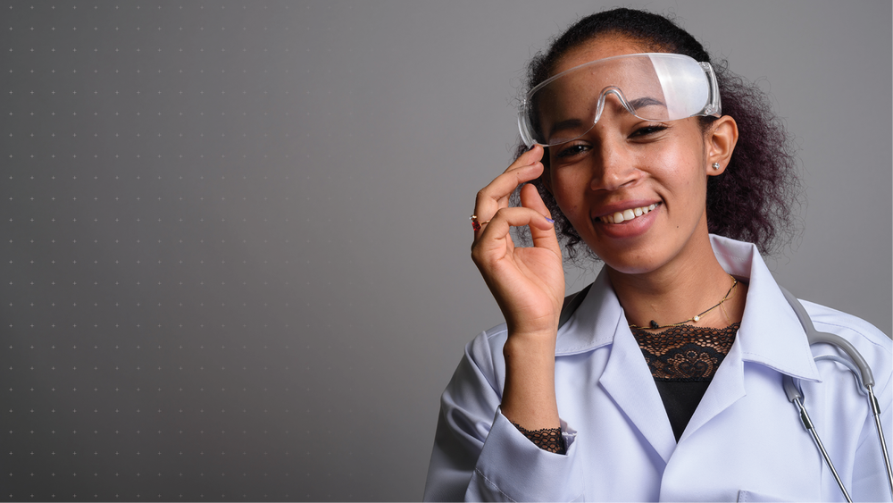 Smiling teenager wearing a lab coat and protective goggles.