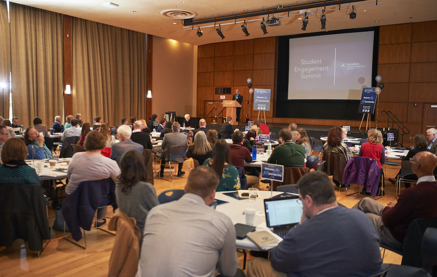 An audience sits at tables in the HUB Alumni room during presentation