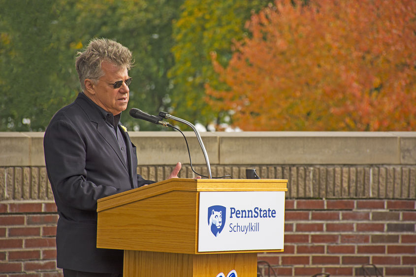 A man wearing all black with sunglasses speaks while standing at a podium