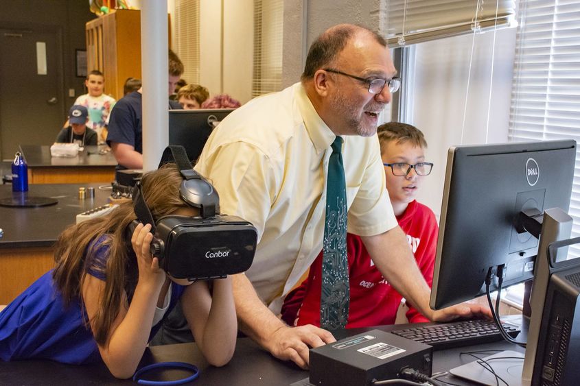 Michael Gallis assists middle schoolers who are trying on VR headsets.