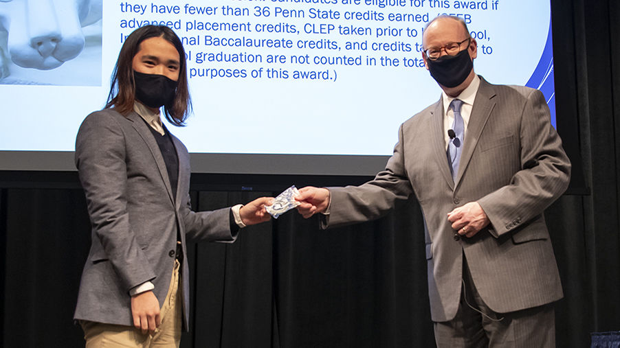 Two men in suits wearing face masks pose for a photo while the man on the right, Chancellor Patrick M. Jones, hands an award to student Pingxu Hao, left.
