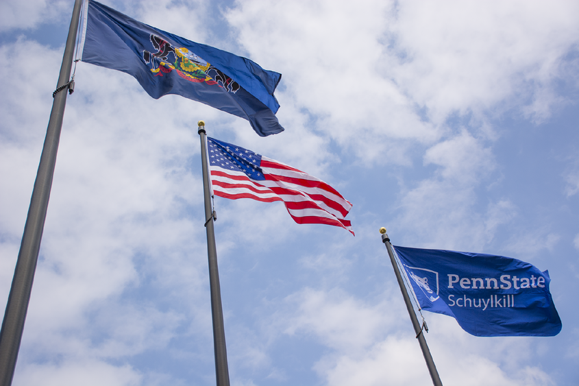 Pennsylvania, U.S., and Penn State Schuylkill flags billow against a blue sky with bright white clouds