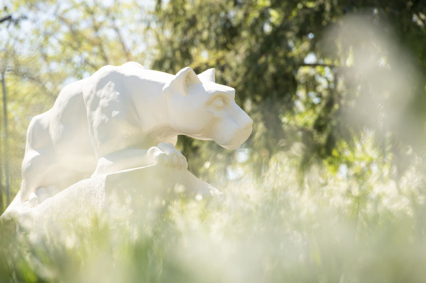 Photo of white Nittany Lion statue through out-of-focus flowers and grass nearby