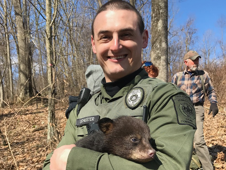 An image of game warden holding a infant bear.